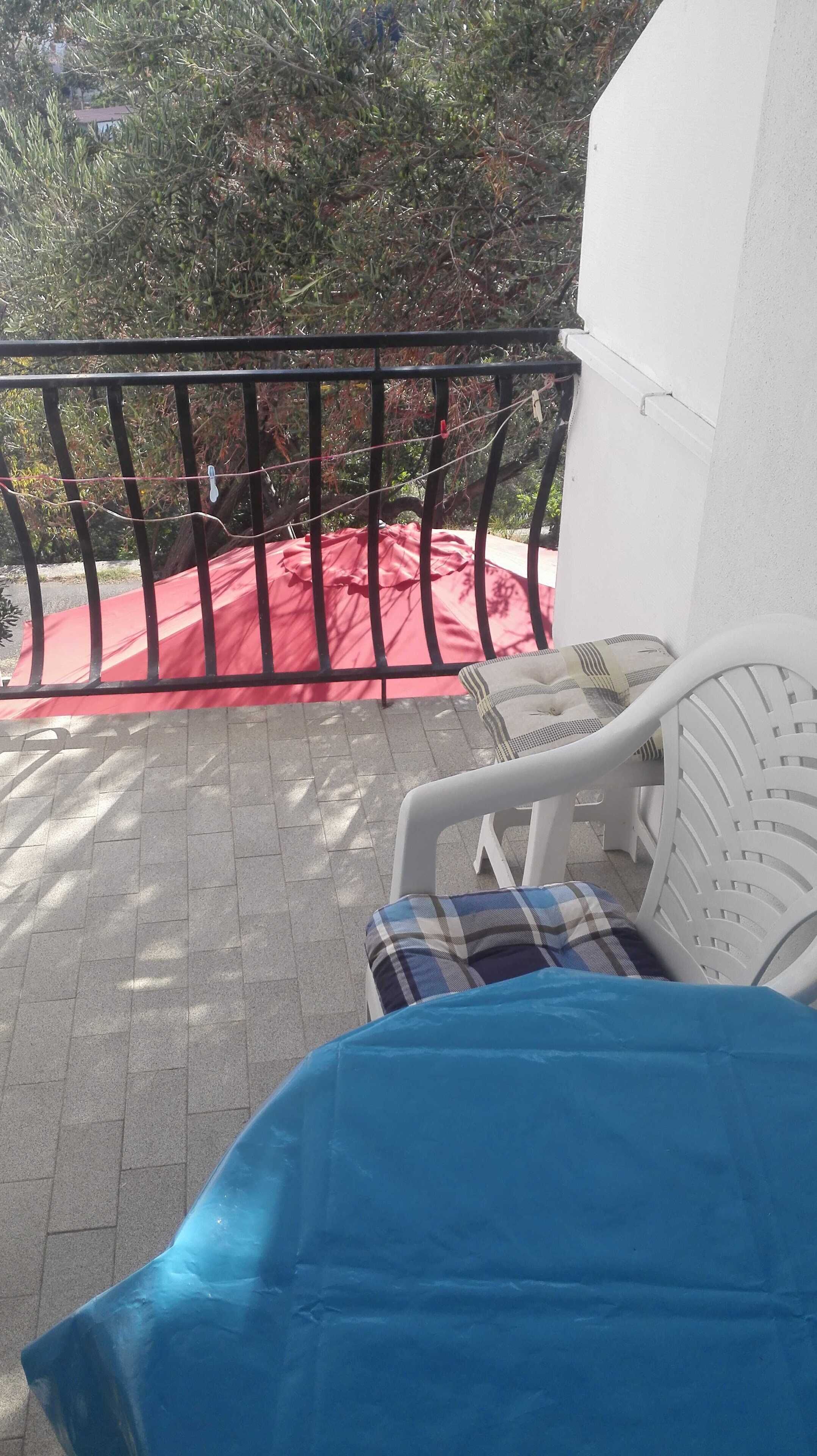 Een balkon met een witte stoel, een rode doek en een zwarte metalen balustrade.