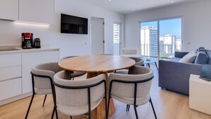 Un apartamento moderno con cocina, comedor y sala de estar. Incluye un televisor de pantalla plana, cafetera y un ventanal con vistas a la ciudad.