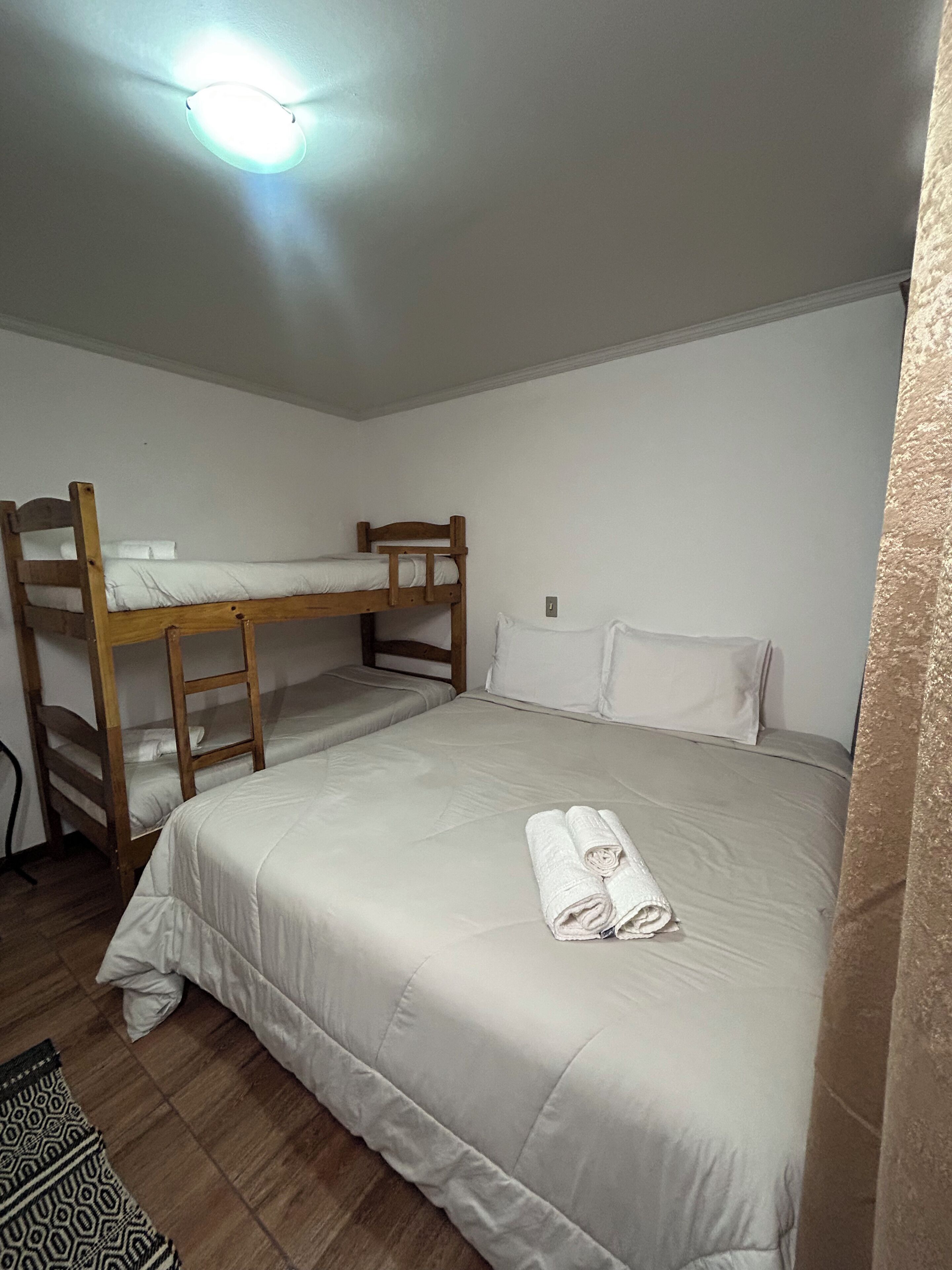A single room with a bunk bed, a neatly made bed with a rolled towel, and a patterned rug on the floor.