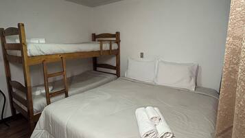 A single room with a bunk bed, a neatly made bed with a rolled towel, and a patterned rug on the floor.