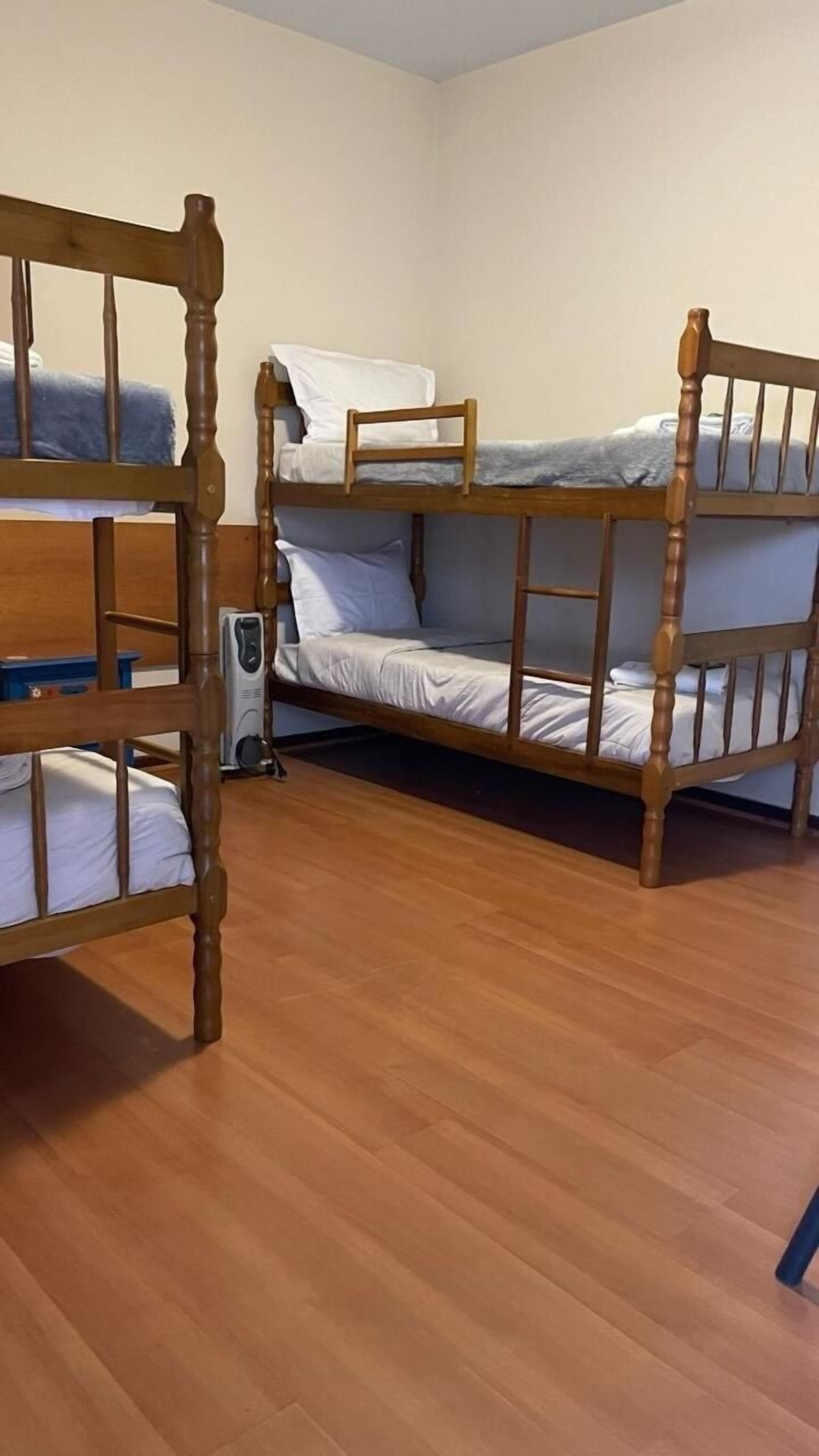 Una habitación con tres literas de madera, un calentador y una silla azul.