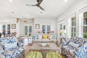 A spacious living room with a ceiling fan, a sofa set, a coffee table, and a view through large windows. - The Oyster Cottage 580 SOU (Port Aransas)