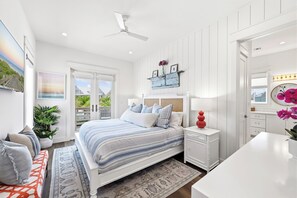 Ein modernes Schlafzimmer mit einem großen Bett, Nachttischen, einem Deckenventilator und Blick ins Freie.