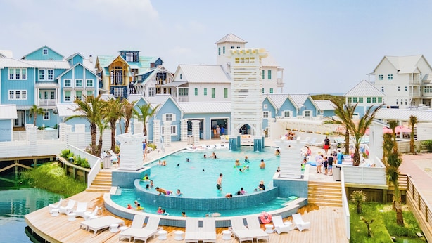 Et resort med en stor swimmingpool omgivet af træterrasser og loungeområder.