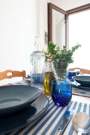 Una mesa de comedor con platos, cubiertos, una botella de vidrio, un florero azul con flores y un mantel a rayas.