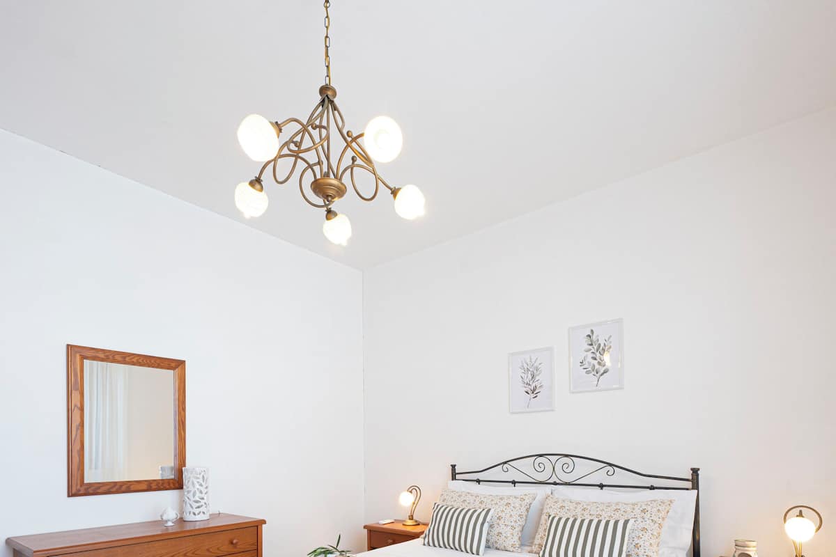 Un dormitorio con cama, cómoda, espejo, un jarrón verde y una araña.