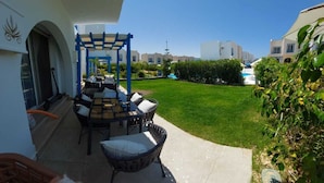 Eine Terrasse mit Tisch und Stühlen, einer Pergola und Blick auf ein Schwimmbad sowie Gebäude im Hintergrund.