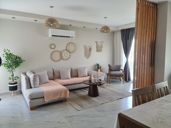 Un salon moderne comprenant un canapé, une table basse, un fauteuil, une plante en pot et des éléments de décoration murale.