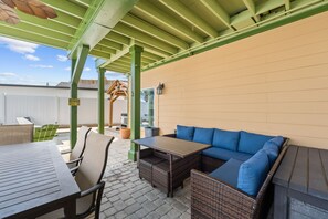 Un espace patio extérieur avec une table en bois, un canapé en osier doté de coussins bleus et une structure de pergola verte.