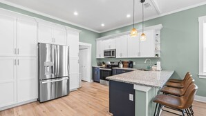 A modern kitchen with white cabinets, stainless steel appliances, a granite countertop, and a bar area with stools. - Seaside Escape  Walk to Beach  Private Pool + Hot Tub (Panama City Beach)