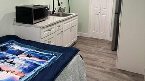 Ein Schlafzimmer mit einem Bett, einem Deckenventilator, einer Klimaanlage, einer Mikrowelle, einem Spülbecken und einem Kühlschrank.
