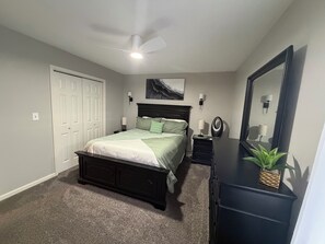 Un dormitorio con cama, cómoda, espejo, ventilador de techo y una puerta.