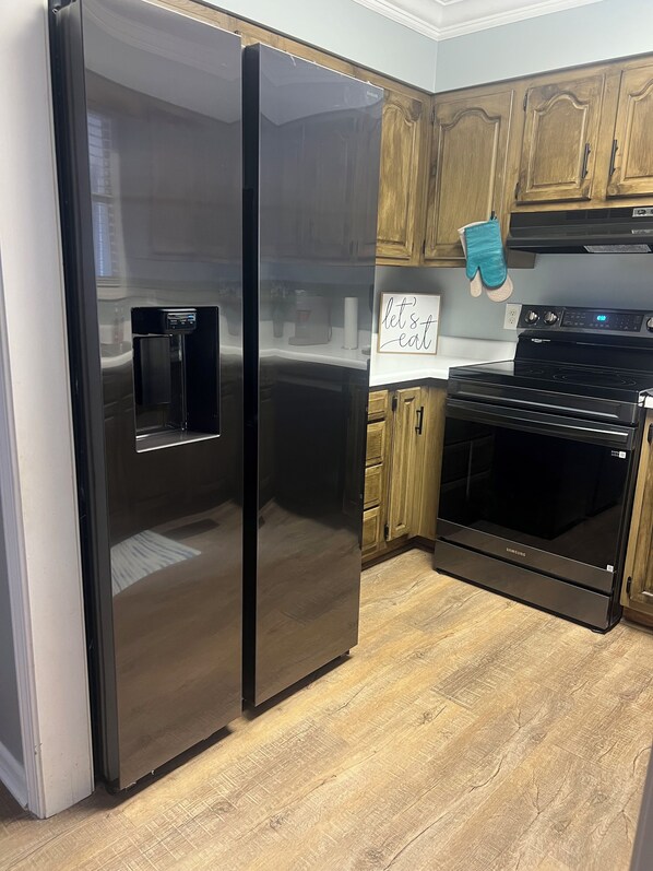 A kitchen with a stainless steel refrigerator, a black oven, wooden cabinets, and a sign that says 'let's eat'.