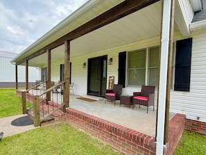 A covered porch with outdoor seating, a staircase leading to the entrance, and a well-maintained lawn.