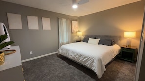 A bedroom with a bed, two bedside tables, a ceiling fan, and a window with curtains.