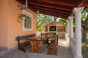 An outdoor patio with a stone oven, wooden furniture, and a pergola structure.