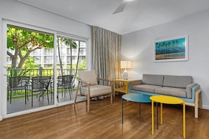 A room with a sliding glass door leading to a balcony, a sofa, a small table, a chair, and a lamp. - Worldmark Kihei (Kihei)