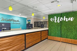 A reception area with a wooden counter, a green wall with 'Aloha' written on it, and a ceiling with recessed lighting.