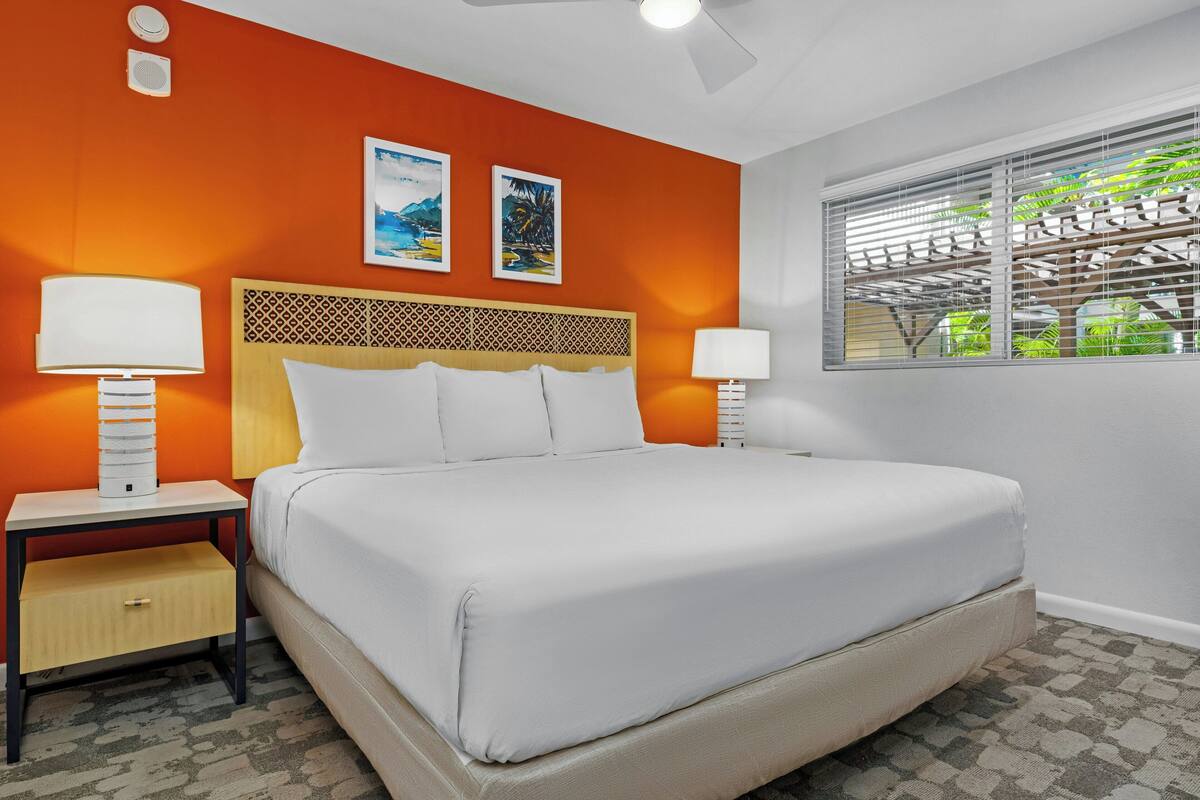 Ein Hotelzimmer mit einem Bett, zwei Nachttischen mit Lampen, einem Kopfteil und zwei gerahmten Bildern an der Wand.