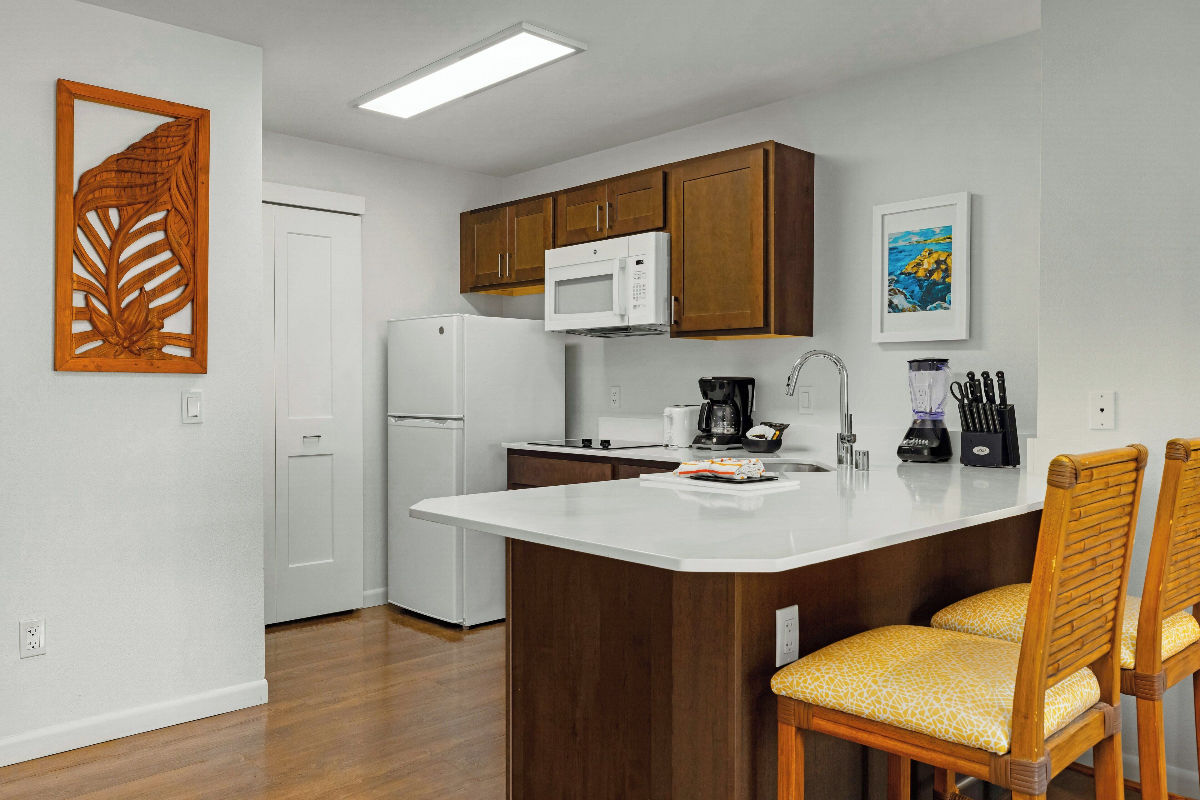 Una cocina con armarios de madera, un refrigerador blanco, un microondas, una cafetera y una licuadora sobre la encimera.