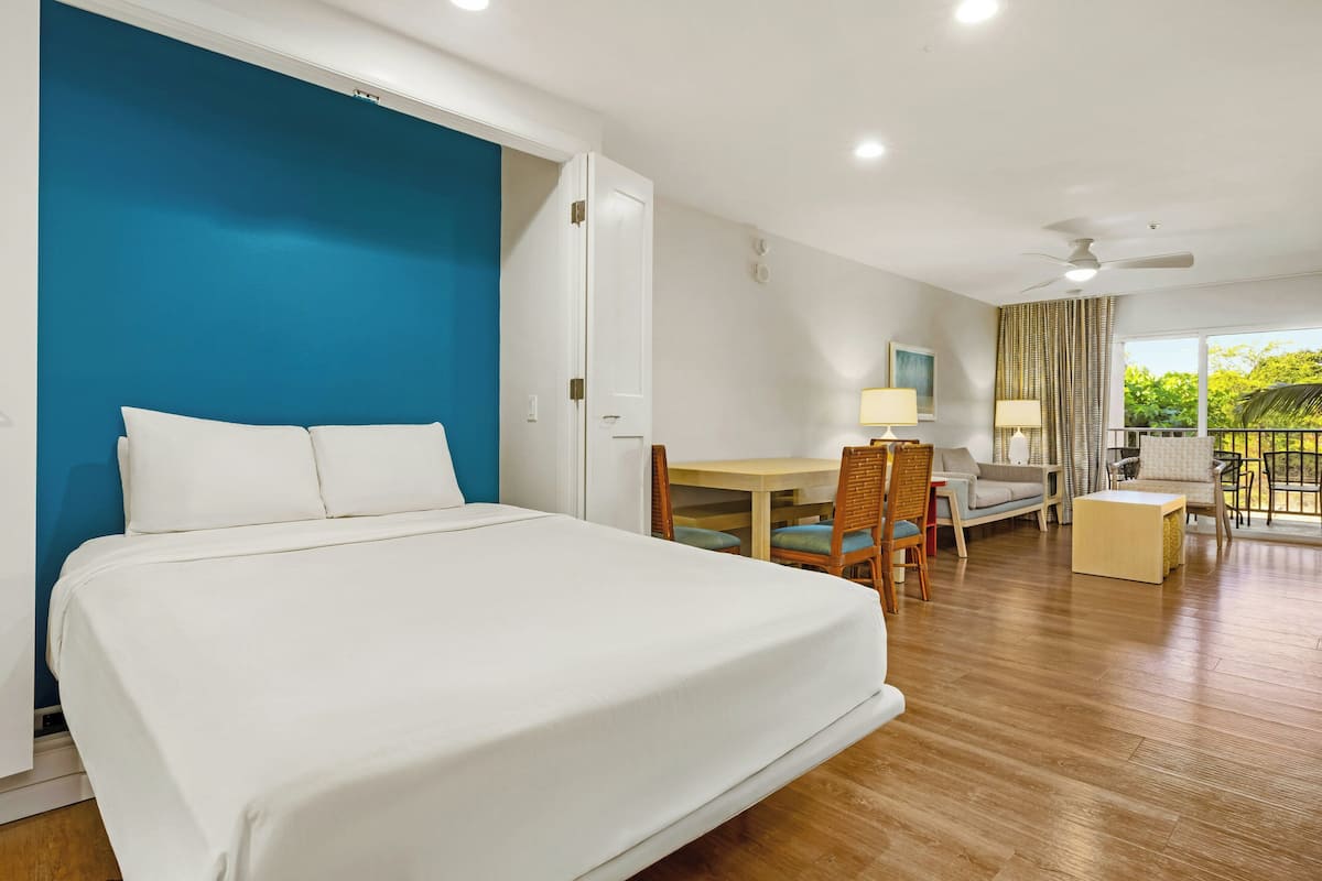 Ein Hotelzimmer mit Bett, Schreibtisch, Stuhl, Sofa und einem Balkon mit Blick.