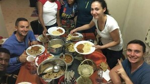 Un grup de persones assegudes al voltant d'una taula plena de plats i estris, suggerint un ambient de sopar compartit.