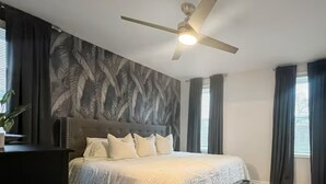 A bedroom with a bed, a ceiling fan, and a window with curtains.