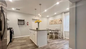 A modern kitchen with a central island, white cabinetry, and a dining area with a glass table and chairs.