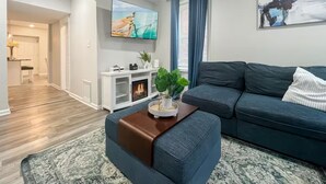 A modern living room with a dark blue sofa, a coffee table with a plant, a flat-screen TV, and a fireplace.