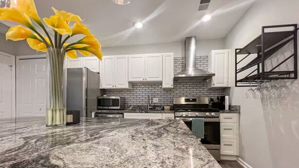 A modern kitchen with white cabinets, a granite countertop, and a stainless steel range hood.