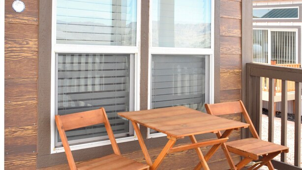 A wooden deck with a table and chairs, large windows, and a railing.