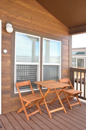Una terraza de madera con una mesa, sillas, ventanas grandes y una barandilla.
