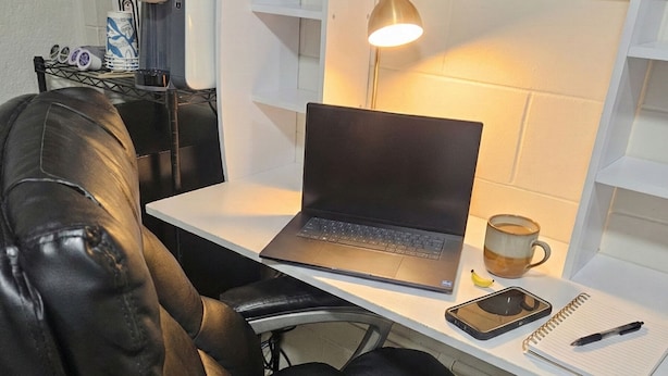 Un espacio de trabajo pequeño con una computadora portátil, una lámpara de escritorio, una libreta y una taza.