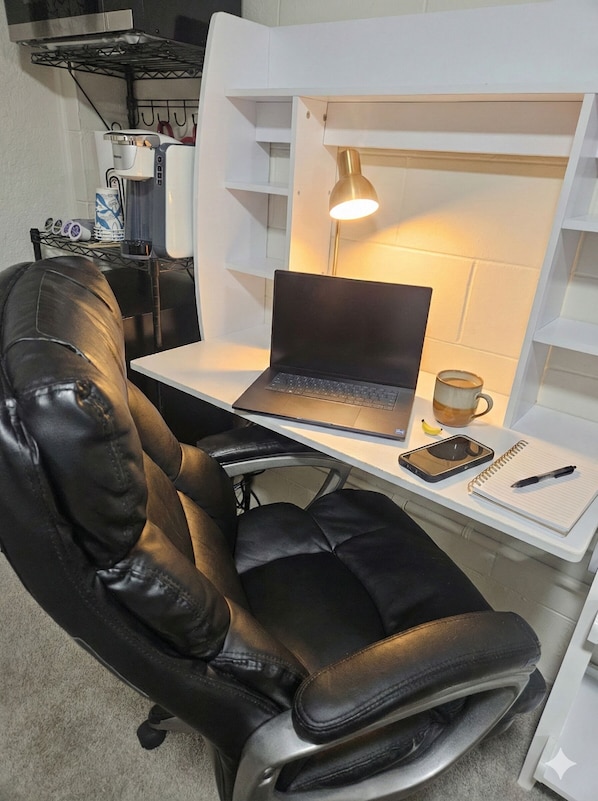A compact workspace with a laptop, a desk lamp, a notebook, and a cup.