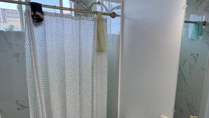 A bathroom with a shower, toilet, and sink, marble walls, and a window with a view. - Kalihi Stream, Coffee Bar, Ro Water, Split Ac, WIFI, Black Out Curtain, 4Parking (Honolulu)