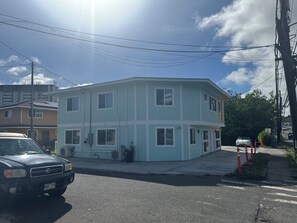 A multi-story building with a light blue exterior, a visible garage door, and a street view with a parked car and a pedestrian crossing.