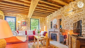 A cozy living room with a stone wall, wooden ceiling beams, a fireplace, and a television. - Gîte des Châtelaines - ANZY LE DUC (ANZY LE DUC)