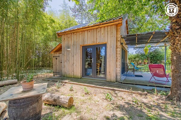 Una cabaña de madera con puerta corrediza de vidrio, una terraza con mobiliario exterior y un bosque de bambú que la rodea.