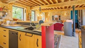 A rustic kitchen with stone walls, wooden beams, and a large island with a sink and dishwasher. - Gîte des Châtelaines - ANZY LE DUC (ANZY LE DUC)