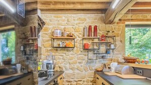 A rustic kitchen with stone walls and wooden beams, equipped with modern appliances and shelves for storage. - Gîte des Châtelaines - ANZY LE DUC (ANZY LE DUC)