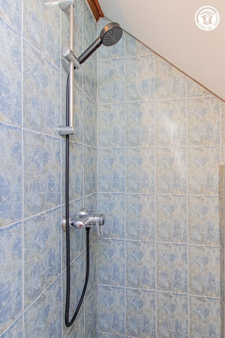 Une douche équipée d’un pommeau de douche à main et d’un flexible, le tout fixé sur un mur carrelé.