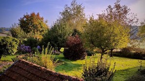 A garden with various plants and trees, a brick structure, and a clear sky. - Gîte du Bois de la Velle (VIRY)