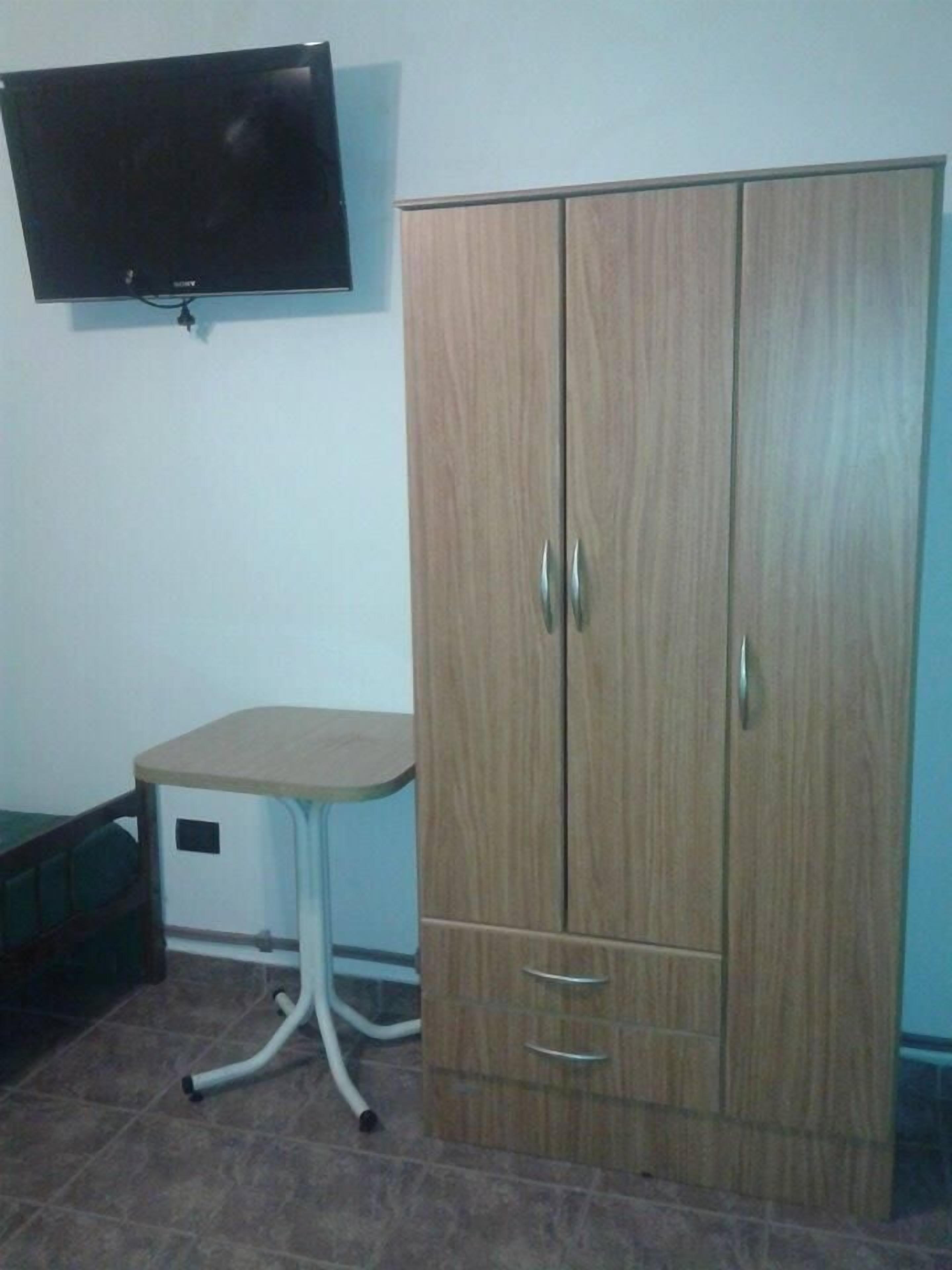 Una habitación con un armario de madera, una mesita pequeña y un televisor montado en la pared.
