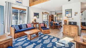 A spacious living area with a high ceiling, a wooden staircase, a sofa set, a dining table, and a kitchen area. - Spacious 5-Bedroom Home Near Beach (Bethany Beach)