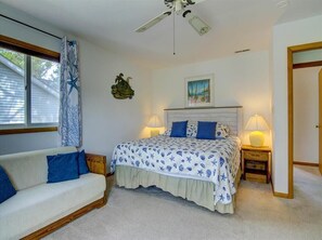 A bedroom with a bed, a nightstand, a lamp, a window with curtains, a ceiling fan, and a wall with a picture.