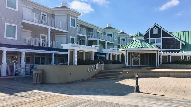 A waterfront property with multiple buildings, a wooden deck, and a green-roofed structure. - Beachfront 3-Bedroom Condo near Shops (Bethany Beach)