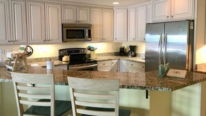 A kitchen with white cabinets, stainless steel appliances, granite countertops, and wooden chairs. - Beachfront 3-Bedroom Condo near Shops (Bethany Beach)