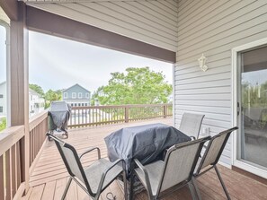 Un espacio al aire libre techado con una mesa, sillas, una parrilla y vistas a casas vecinas.