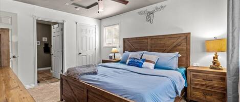 A bedroom with a wooden bed, a ceiling fan, a nightstand with a lamp, and a wall decoration.