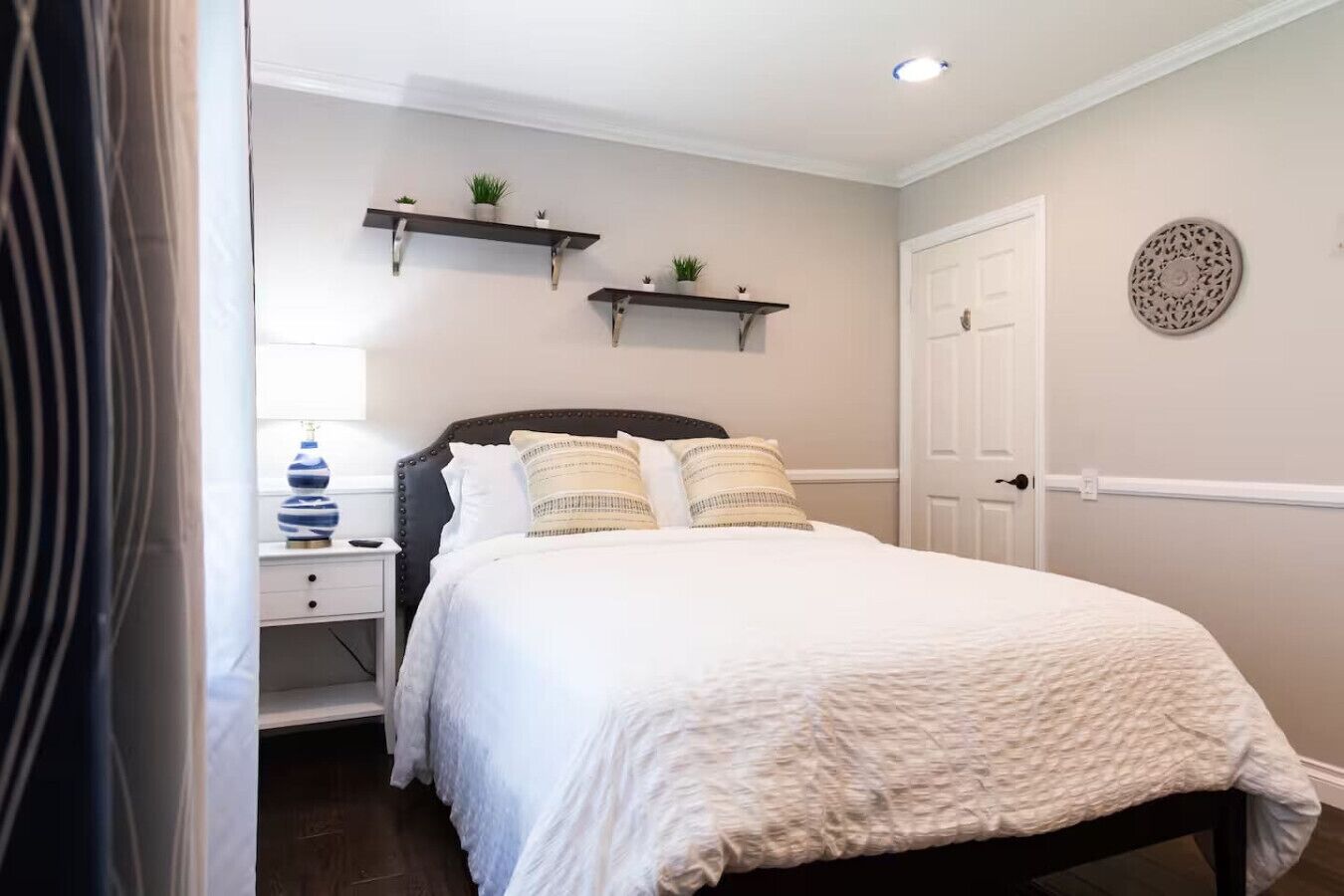 Un dormitorio con cama, mesitas de noche, una mesilla auxiliar y estantes en la pared con plantas.